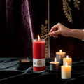 Halloween-Emporium 7 day red candle in a glass jar being lit by a hand with a match against a dark velvet background