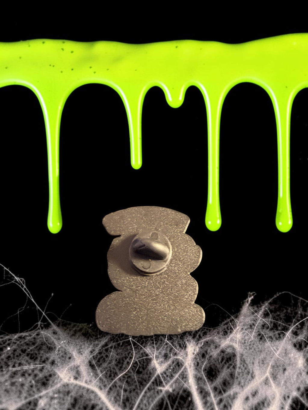Halloween-Emporium Trick 'r' Treat Sam enamel pin back view showing metal clutch against green slime and cobwebs