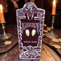 Halloween-Emporium Scarecrow Small Deluxe Fangs in a decorative tombstone-shaped case on a wooden table with candles.