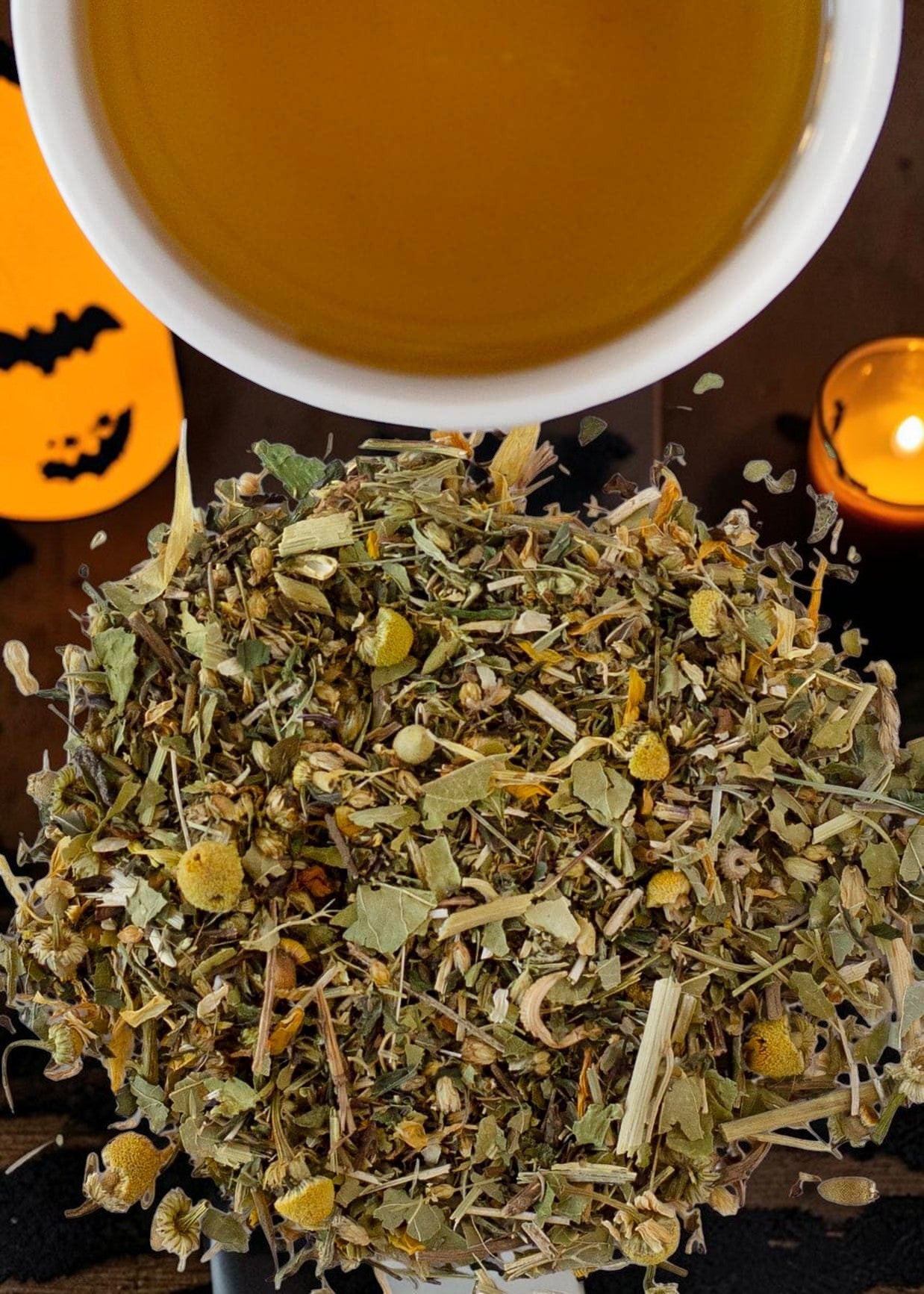 Halloween-Emporium Sleepy Wellness herbal tea blend with chamomile and dried herbs next to a cup of tea and candle