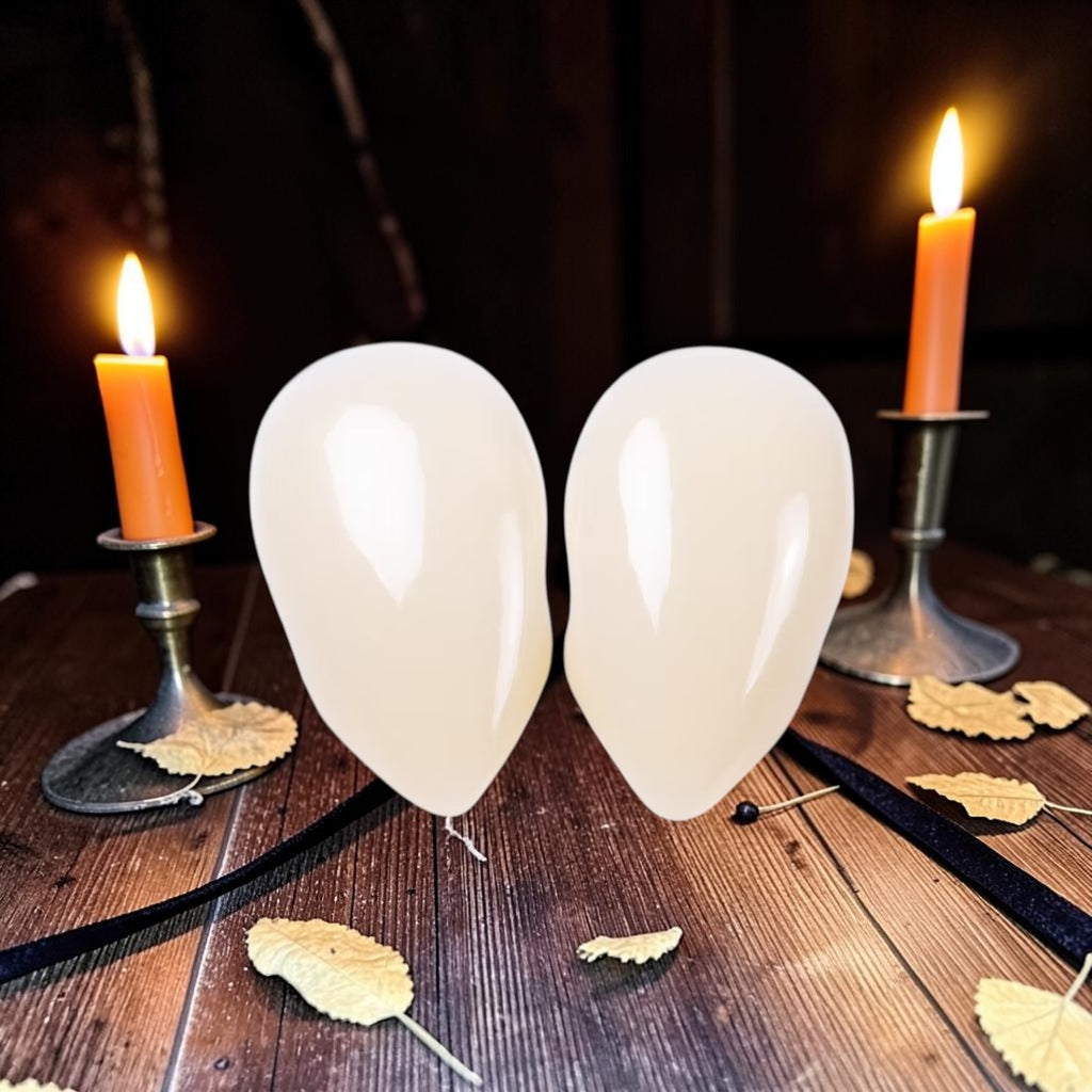 Halloween-Emporium small deluxe vampire fangs in natural off-white color, displayed on a wooden table with candles.