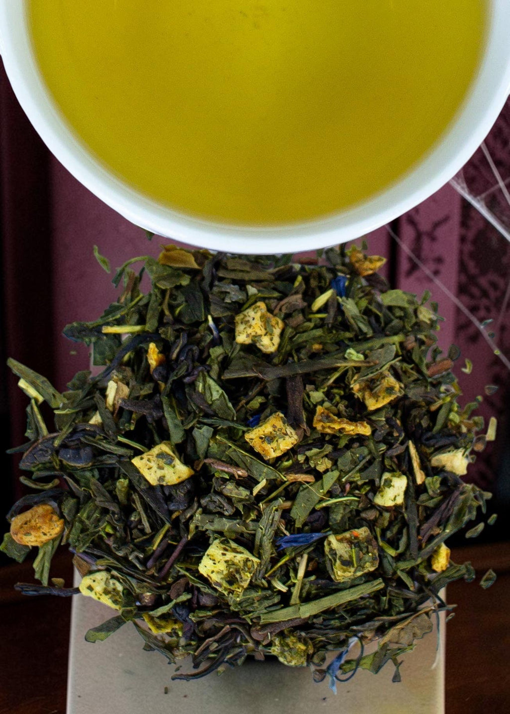 Halloween-Emporium Grim Grinning Green spiced apple green tea blend with dried fruit and spices next to a cup of tea.