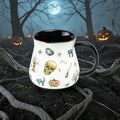 Halloween-Emporium stoneware mug with spooky skull and cat pattern, black interior, and gold rim in a forest setting.