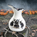 Halloween-Emporium stoneware witches brew pitcher with black interior, raven and cauldron art, and gold detailing.