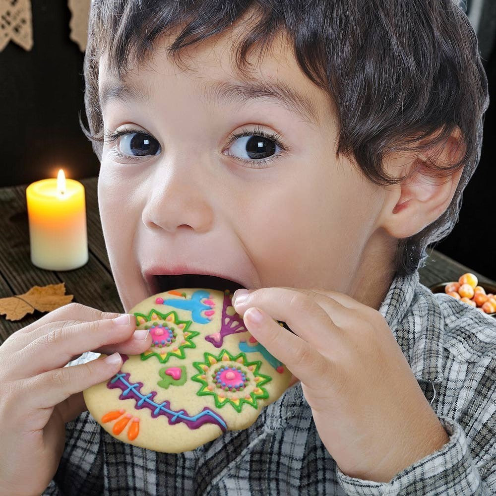 A young boy eating a colorful sugar skull cookie made with Halloween-Emporium Sweet Spirits cookie cutters.