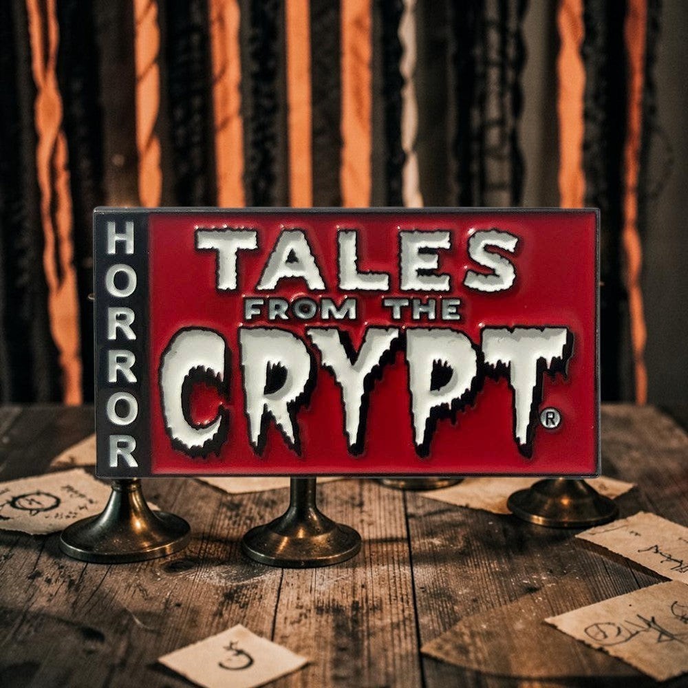 Halloween-Emporium Tales From The Crypt enamel pin featuring a red background and white logo on a wooden table.