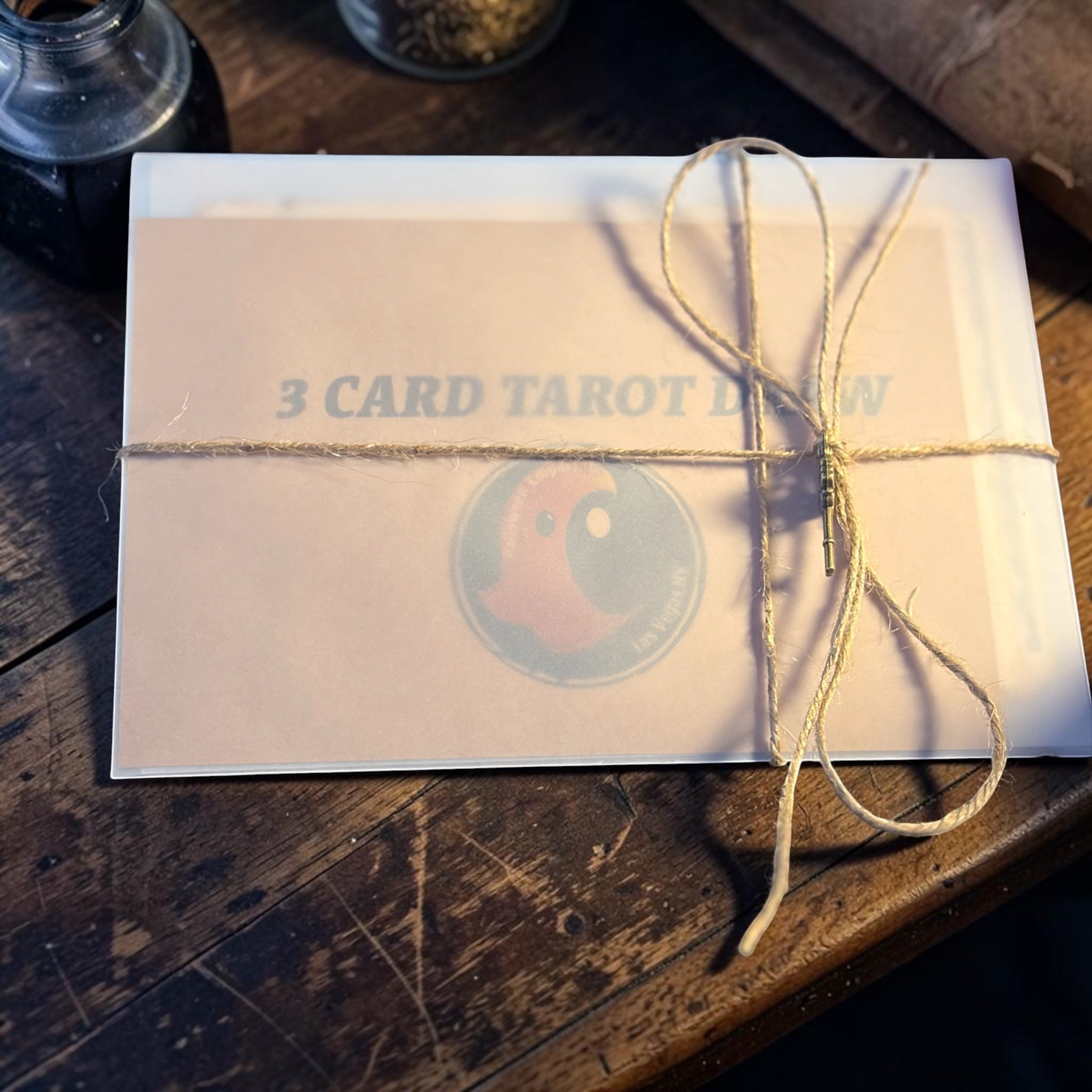 Halloween-Emporium 3 card tarot draw set in a semi-translucent envelope tied with rustic twine on a wooden table.