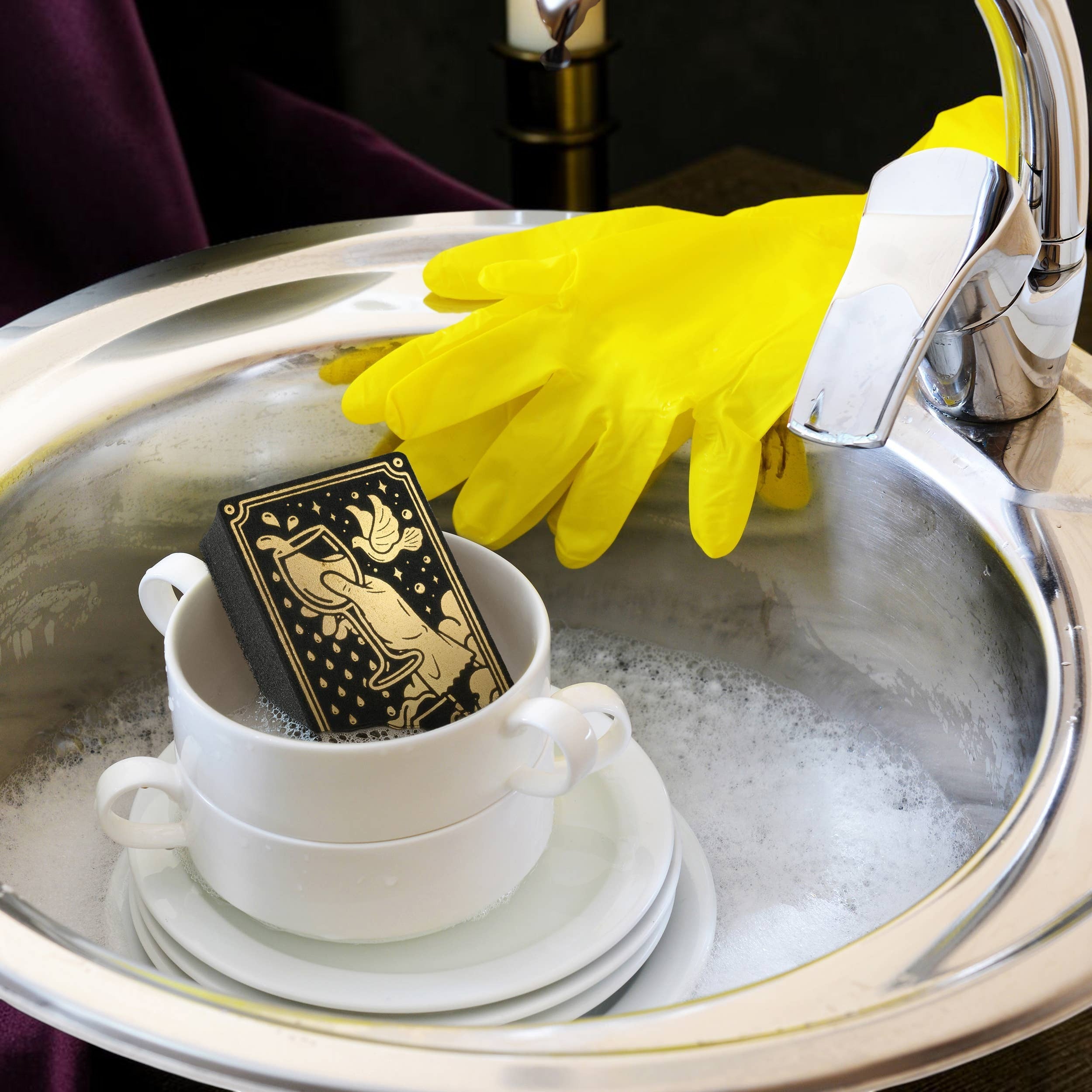 Halloween-Emporium tarot card sponge with gold Ace of Cups design in a soapy kitchen sink with yellow rubber gloves