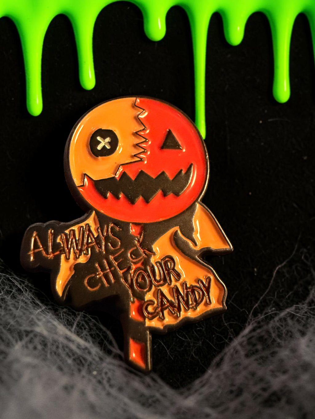 Halloween-Emporium Trick 'r' Treat enamel pin featuring Sam's lollipop and the Always Check Your Candy motto.