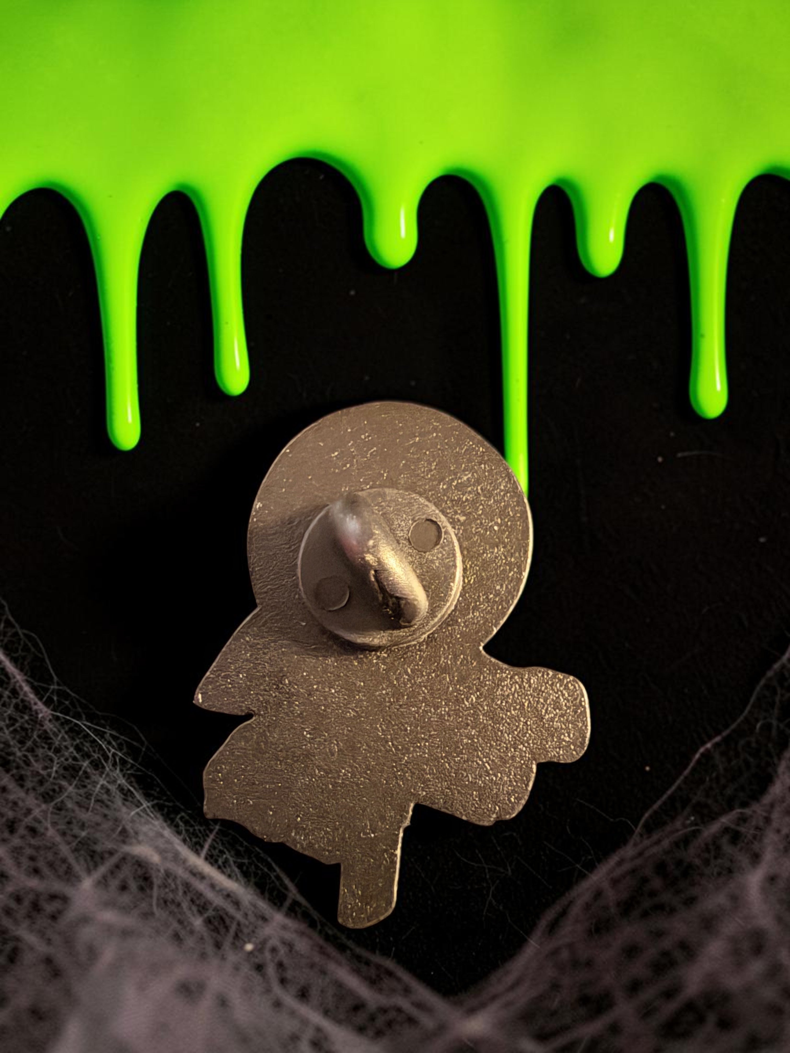 Halloween-Emporium Trick 'r' Treat enamel pin back view showing metal clasp against black background with green slime