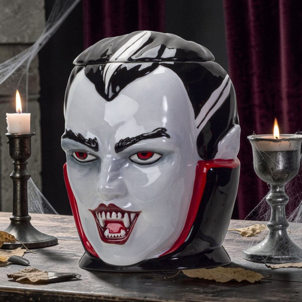 Halloween-Emporium vampire ceramic treat jar with glossy finish, red eyes, and fangs on a wooden table with candles.
