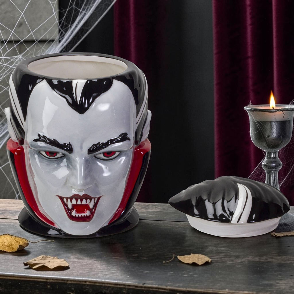Halloween-Emporium vampire ceramic treat jar with glossy finish, red eyes, and fangs, displayed on a dark table.
