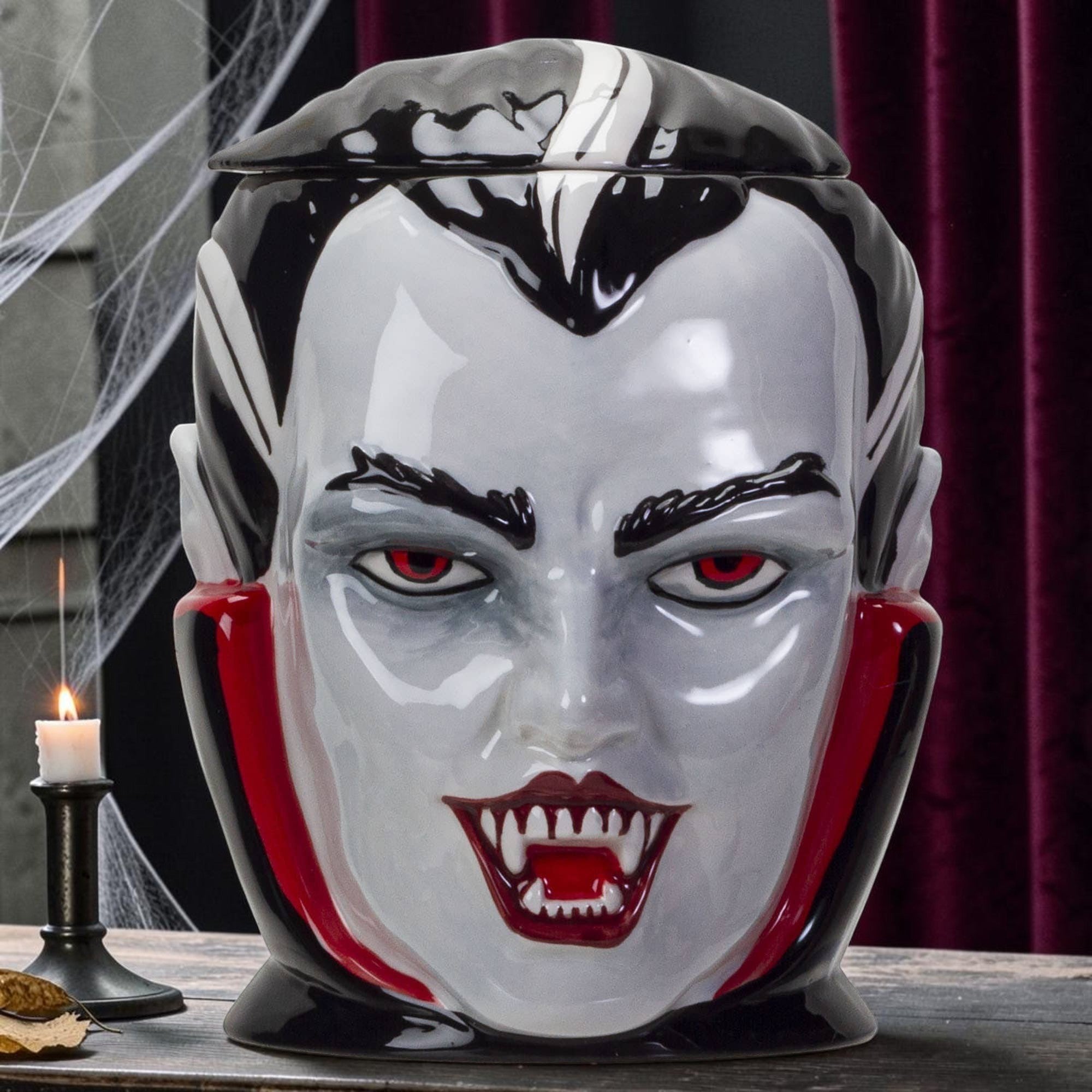Halloween-Emporium vampire ceramic treat jar with red eyes, sharp fangs, and a glossy black and white finish.