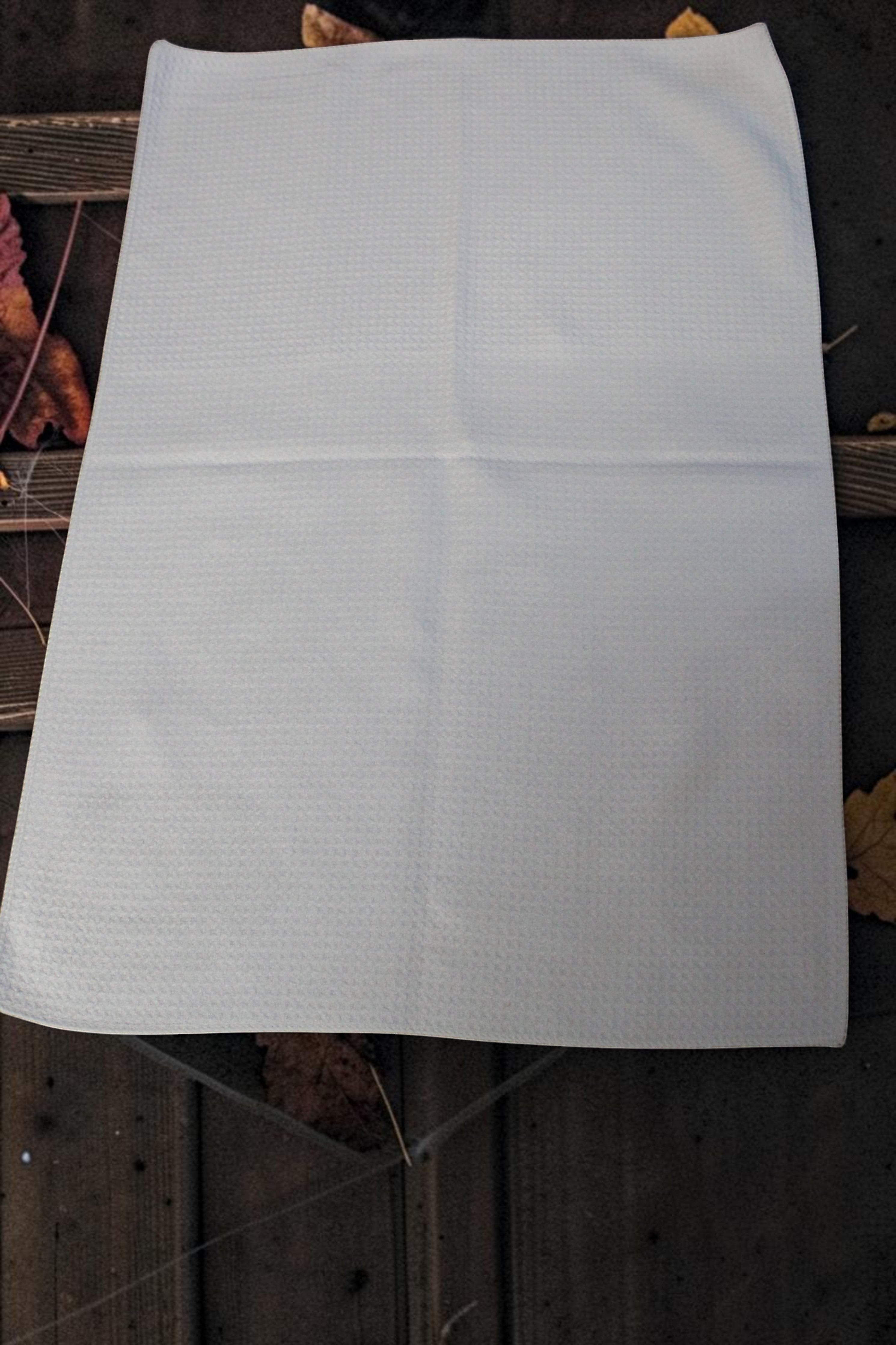 Halloween-Emporium white waffle-weave kitchen dishcloth laid flat on a rustic wooden surface with autumn leaves.