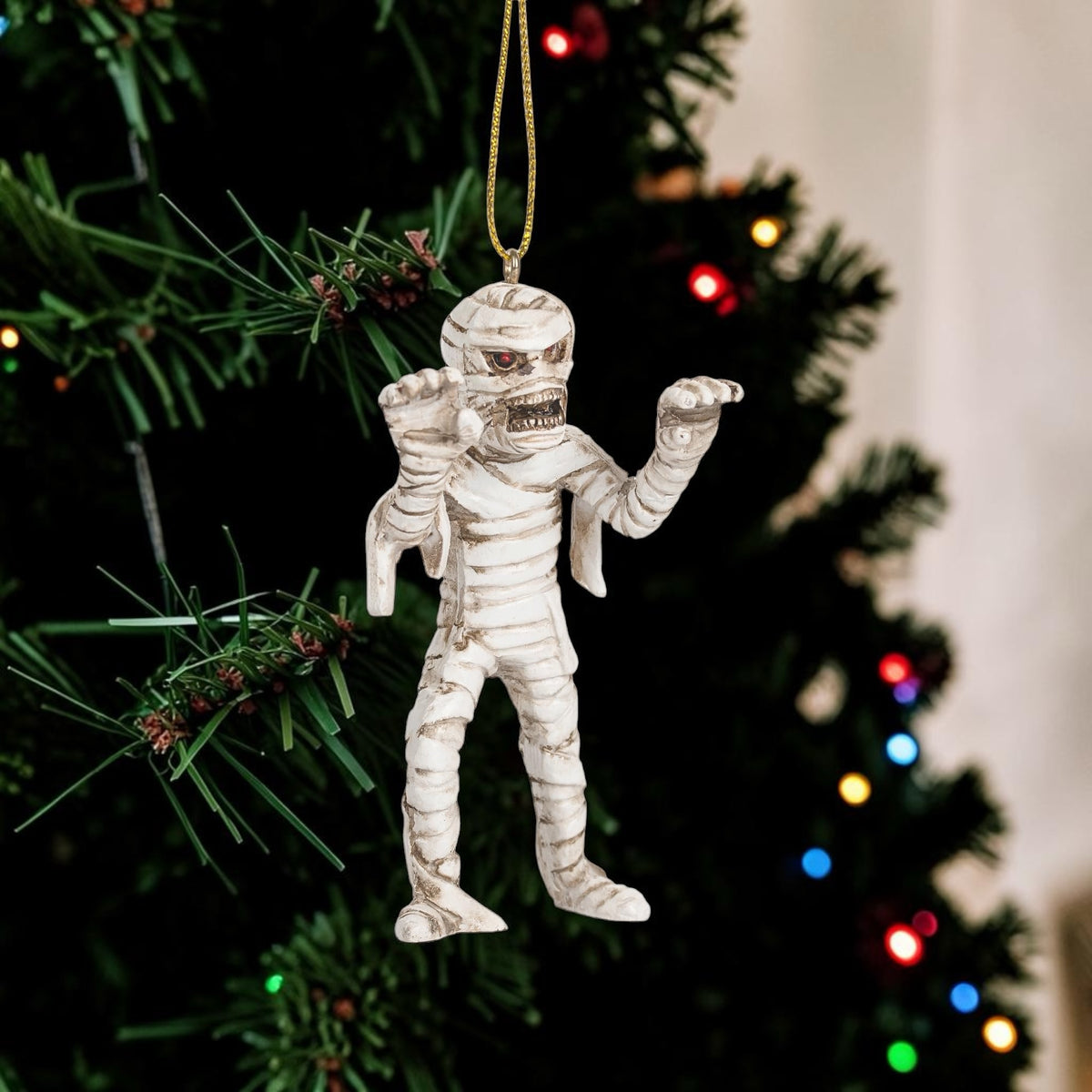 Halloween-Emporium mummy hanging ornament with detailed bandages and red eyes on a Christmas tree.
